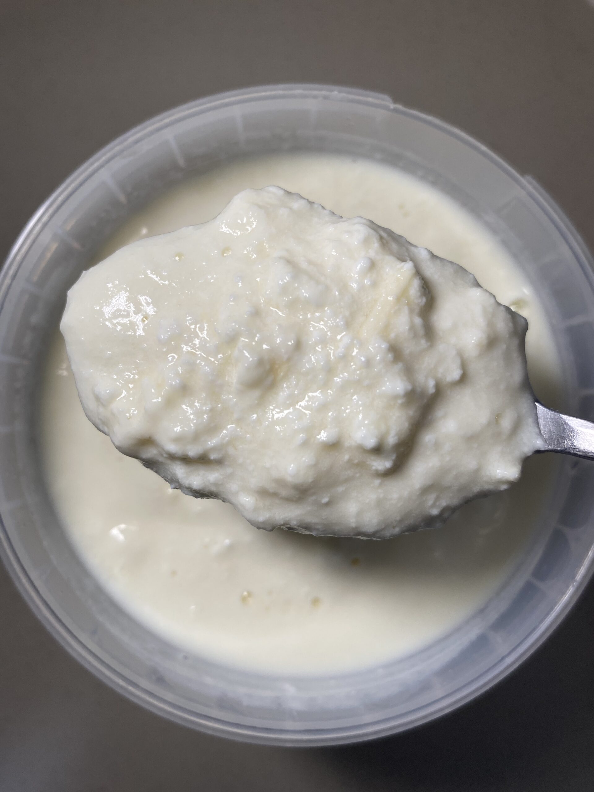Close-up of homemade yogurt on a spoon over a container, showing thick and creamy texture.